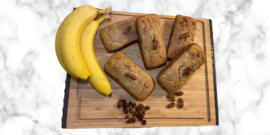 Banana Bread next to a bunch of bananas on a wood cutting board.