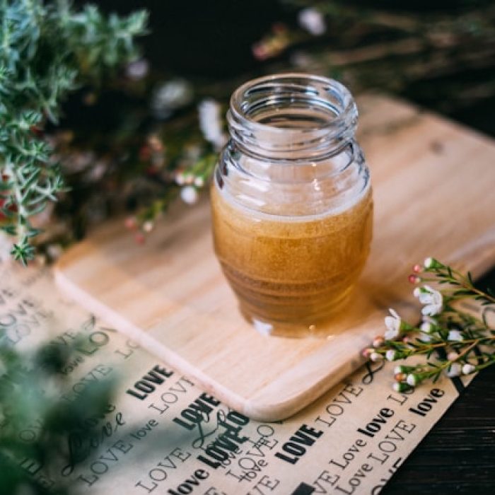 Jar of honey on a cutting board, surrounded by herbs.