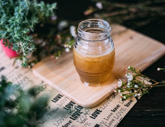 Jar of honey on a cutting board, surrounded by herbs.