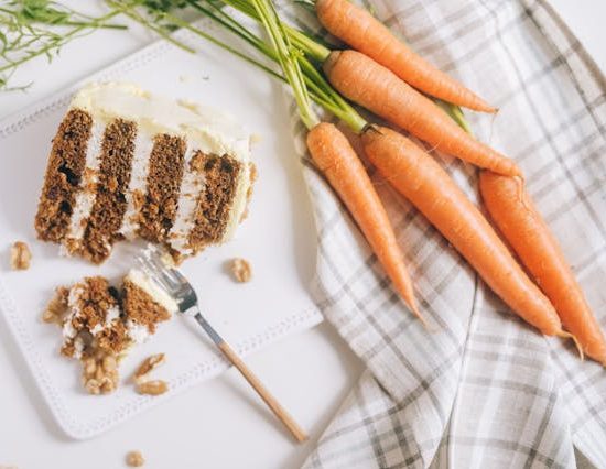 Carrot cake next to a bunch of carrots.